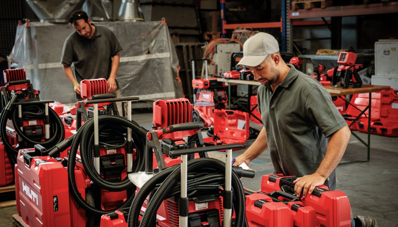 Un comercial de Hilti con un cliente en su almacén con maletinesas de herramientas Hilti a su alrededor 